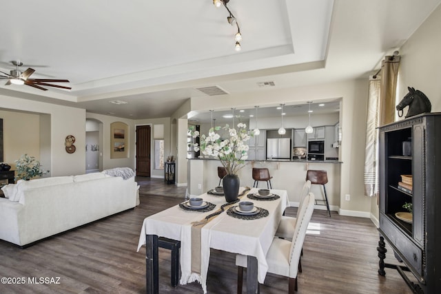 dining area featuring dark hardwood / wood-style flooring, rail lighting, a raised ceiling, and ceiling fan