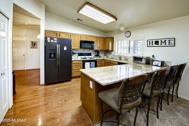 kitchen featuring lofted ceiling, sink, a kitchen breakfast bar, kitchen peninsula, and black appliances