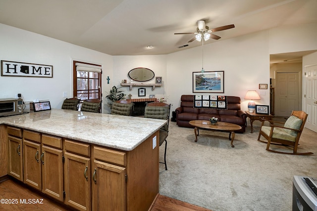 kitchen featuring light stone countertops, carpet, ceiling fan, and kitchen peninsula