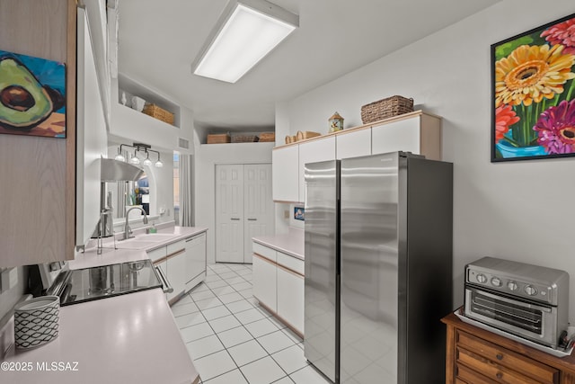 kitchen with stainless steel refrigerator, sink, white cabinets, stove, and light tile patterned floors