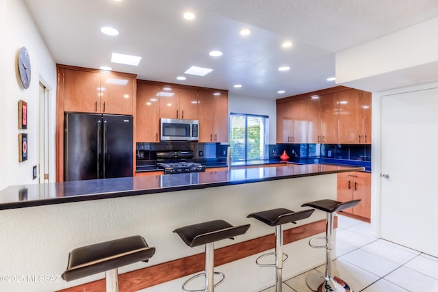 kitchen with black fridge, range, light tile patterned floors, kitchen peninsula, and backsplash