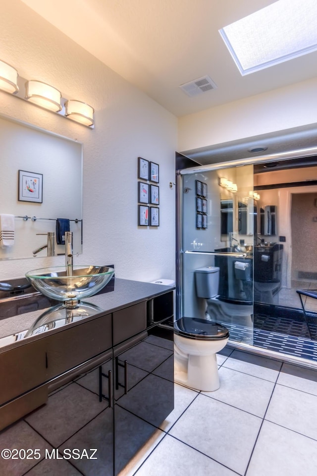 bathroom featuring tile patterned flooring, vanity, a skylight, and toilet