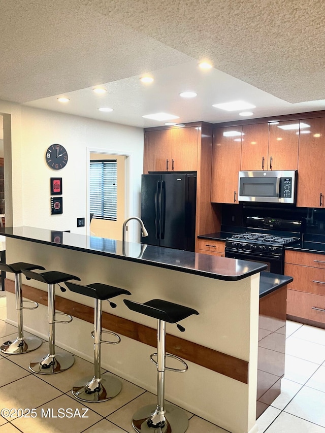 kitchen featuring light tile patterned flooring, a kitchen breakfast bar, a textured ceiling, and black appliances