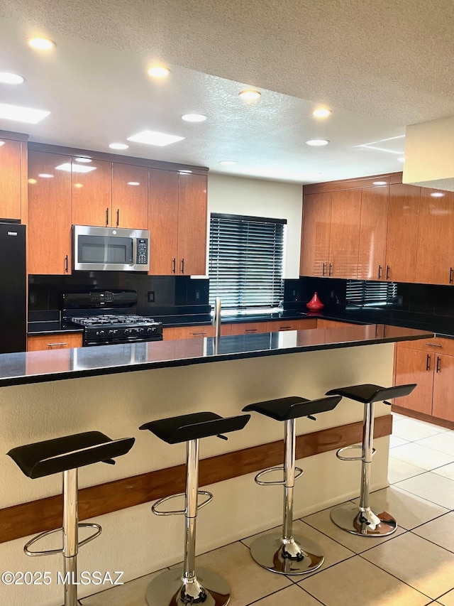 kitchen featuring black range with gas cooktop, a kitchen breakfast bar, a textured ceiling, and light tile patterned floors