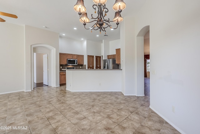 kitchen with baseboards, a high ceiling, arched walkways, appliances with stainless steel finishes, and brown cabinets