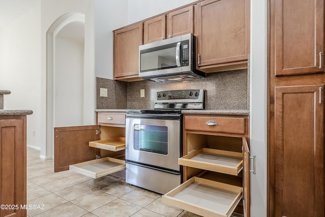 kitchen with brown cabinetry, stainless steel appliances, light tile patterned flooring, and decorative backsplash