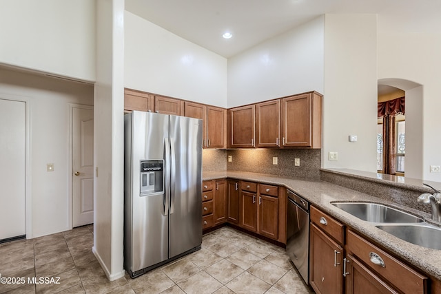 kitchen with light tile patterned floors, brown cabinetry, a sink, stainless steel appliances, and a towering ceiling