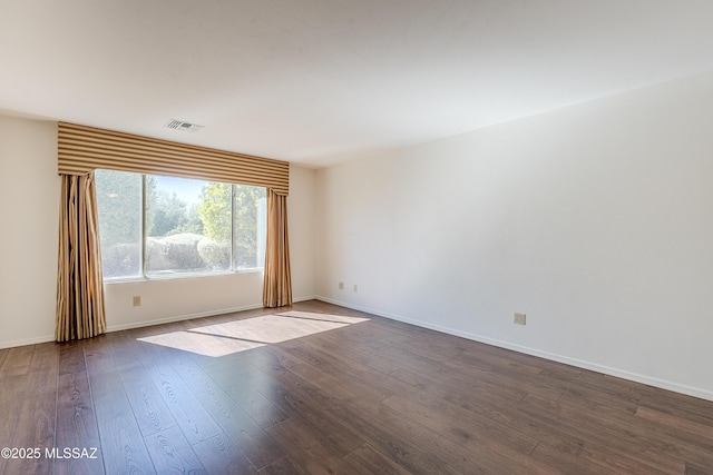 spare room featuring visible vents, baseboards, and dark wood-type flooring