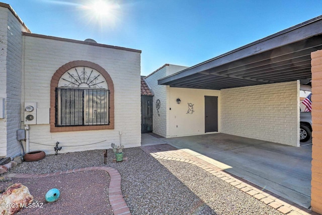 entrance to property with driveway, an attached carport, and brick siding