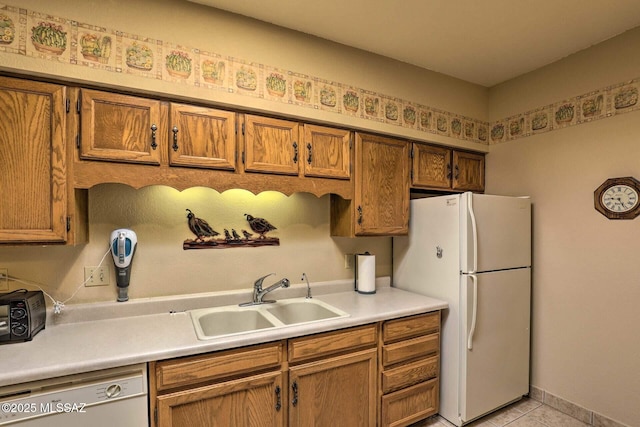 kitchen featuring a sink, light countertops, freestanding refrigerator, dishwasher, and brown cabinetry