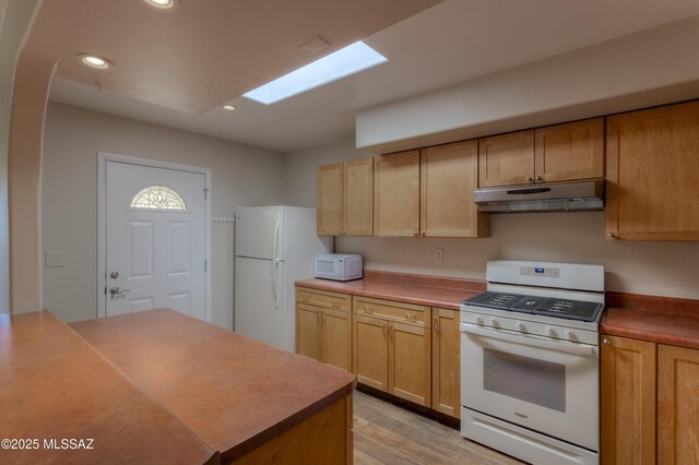 kitchen with sink, white appliances, a skylight, a tray ceiling, and light wood-type flooring