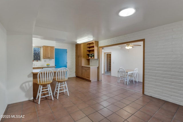 kitchen featuring light tile patterned flooring, brick wall, backsplash, a kitchen breakfast bar, and ceiling fan