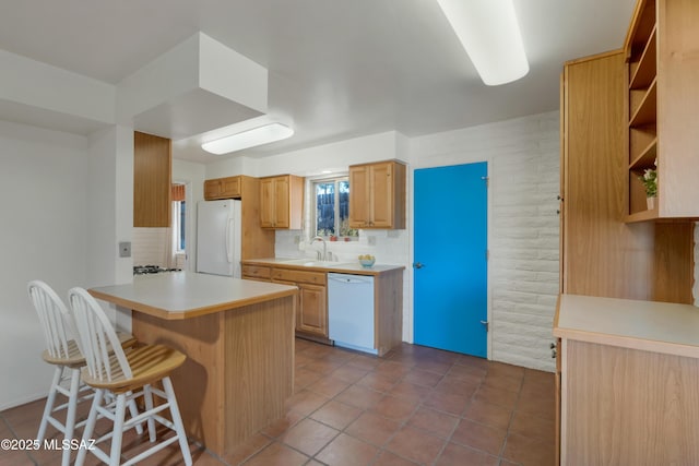 kitchen with a kitchen bar, sink, light brown cabinets, kitchen peninsula, and white appliances