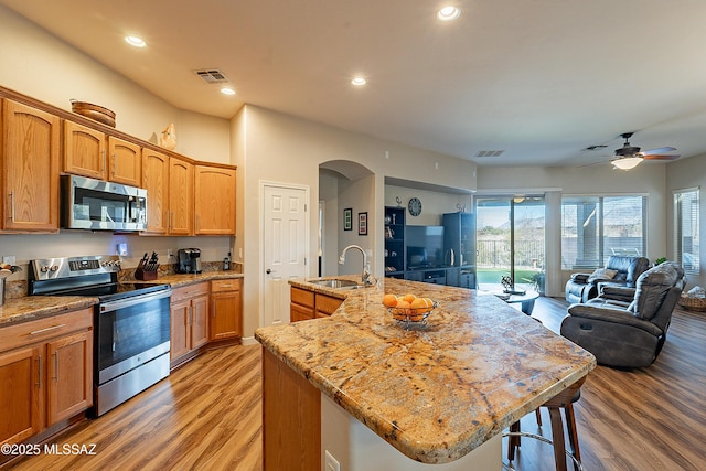 kitchen with sink, light hardwood / wood-style flooring, stainless steel appliances, light stone countertops, and a center island with sink