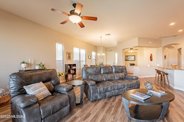 living room featuring ceiling fan with notable chandelier and light wood-type flooring