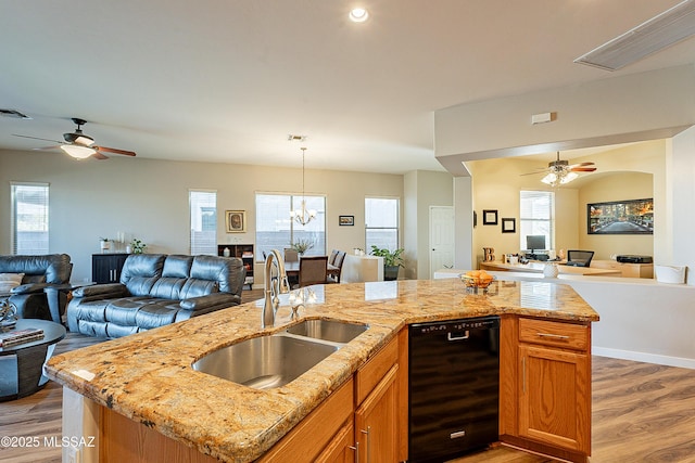 kitchen featuring light stone counters, sink, an island with sink, and black dishwasher