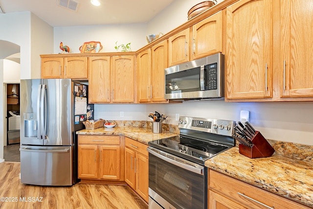 kitchen with appliances with stainless steel finishes, light wood-type flooring, light brown cabinets, and light stone counters