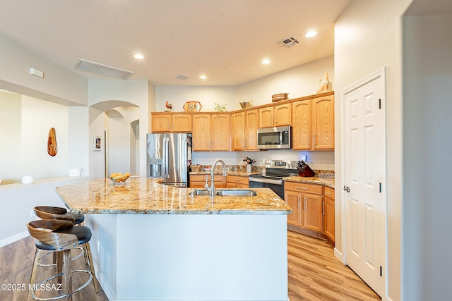 13774 N High Mountain View Pl, Tucson, AZ 85739 - kitchen featuring appliances with stainless steel finishes, a kitchen island with sink, light wood-style floors, arched walkways, and recessed lighting