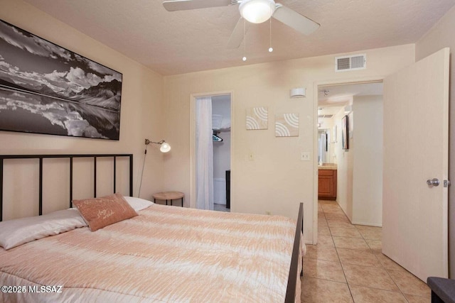 tiled bedroom with ceiling fan, a walk in closet, a closet, and a textured ceiling