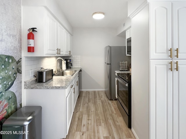 kitchen with appliances with stainless steel finishes, white cabinetry, sink, backsplash, and light wood-type flooring