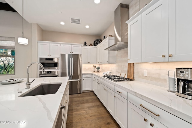 kitchen with stainless steel appliances, decorative light fixtures, light stone counters, and wall chimney exhaust hood