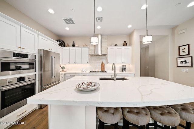 kitchen featuring wall chimney exhaust hood, a kitchen island with sink, and sink