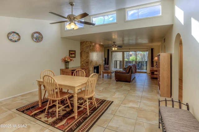 tiled dining space featuring ceiling fan, a towering ceiling, and a tiled fireplace