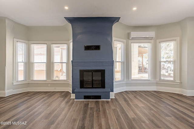 unfurnished living room featuring a fireplace, dark wood-type flooring, a wall unit AC, and a healthy amount of sunlight