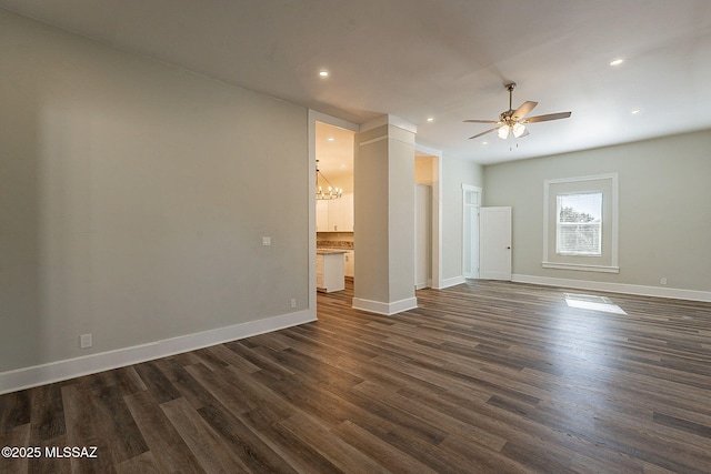 empty room featuring ceiling fan with notable chandelier and dark hardwood / wood-style flooring