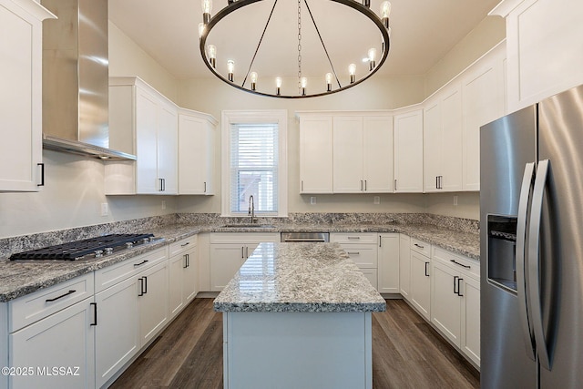 kitchen with appliances with stainless steel finishes, pendant lighting, white cabinets, a center island, and wall chimney range hood