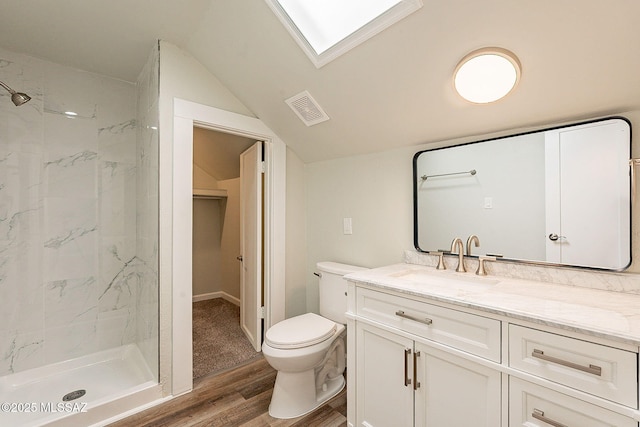 bathroom featuring lofted ceiling with skylight, tiled shower, vanity, wood-type flooring, and toilet