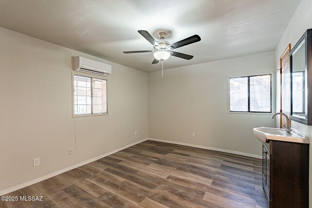 unfurnished room with sink, dark wood-type flooring, a wall mounted air conditioner, and a textured ceiling