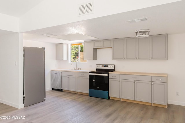 kitchen with appliances with stainless steel finishes, gray cabinets, light hardwood / wood-style floors, and sink