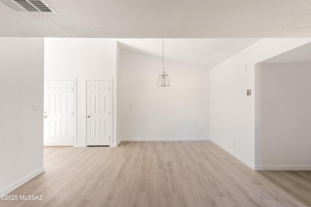 empty room featuring lofted ceiling, light hardwood / wood-style floors, and a textured ceiling