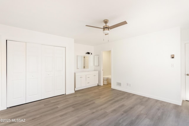 unfurnished bedroom featuring ceiling fan, ensuite bathroom, a closet, and light wood-type flooring