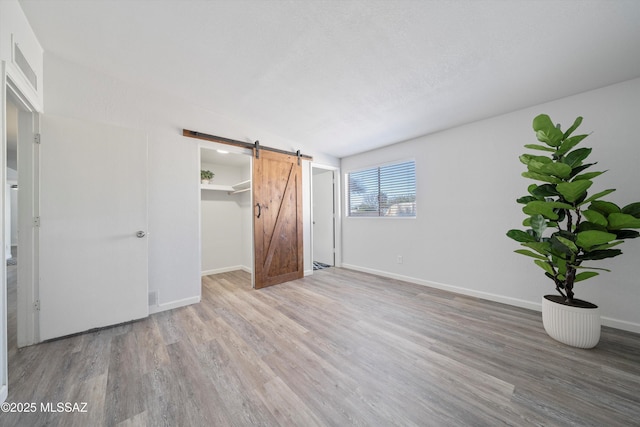 unfurnished bedroom with hardwood / wood-style flooring, lofted ceiling, a barn door, and a spacious closet