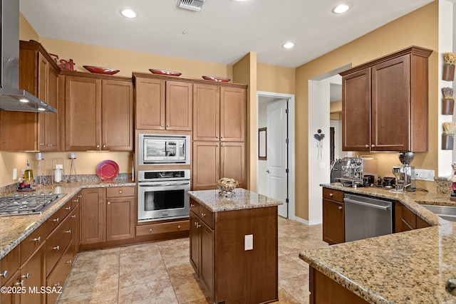 kitchen with wall chimney exhaust hood, appliances with stainless steel finishes, and light stone countertops