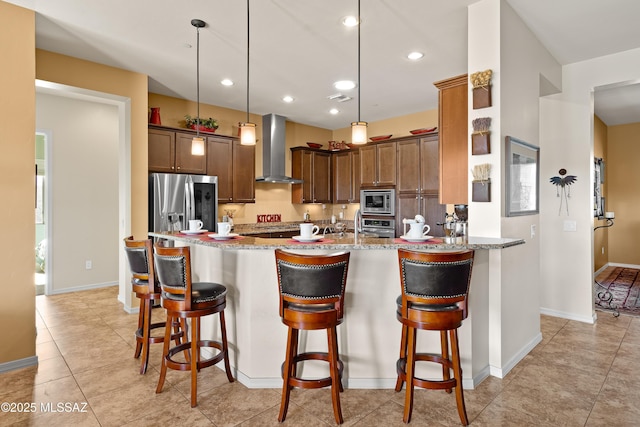 kitchen with wall chimney range hood, a breakfast bar, appliances with stainless steel finishes, light stone counters, and decorative light fixtures