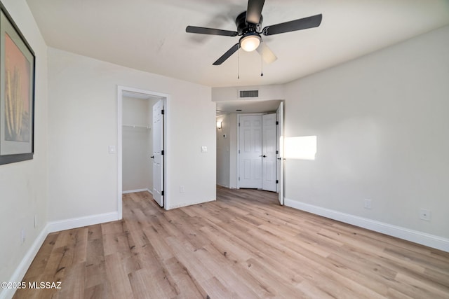 unfurnished bedroom with ceiling fan, a spacious closet, light wood-type flooring, and a closet