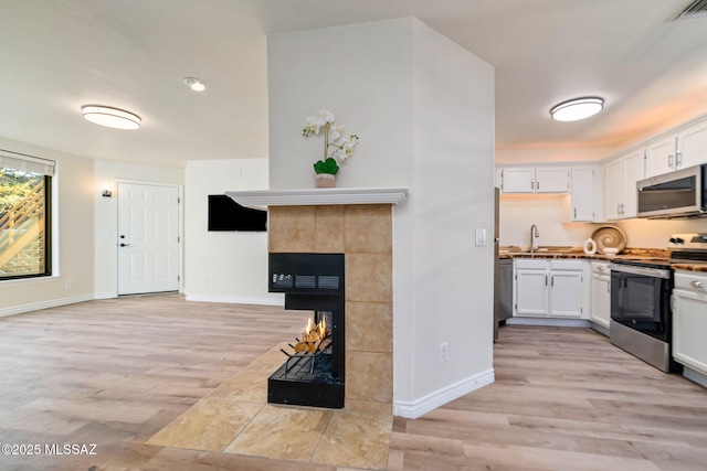 kitchen featuring stainless steel appliances, white cabinets, a fireplace, and light hardwood / wood-style flooring