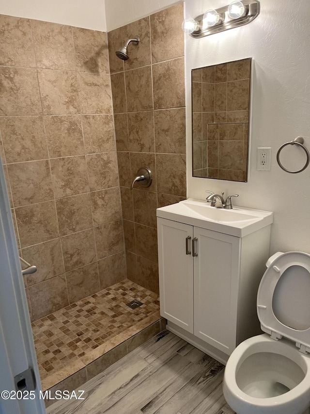 bathroom featuring a tile shower, vanity, hardwood / wood-style floors, and toilet