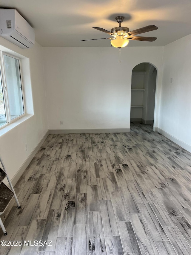 empty room with a wall mounted AC, ceiling fan, and light hardwood / wood-style flooring