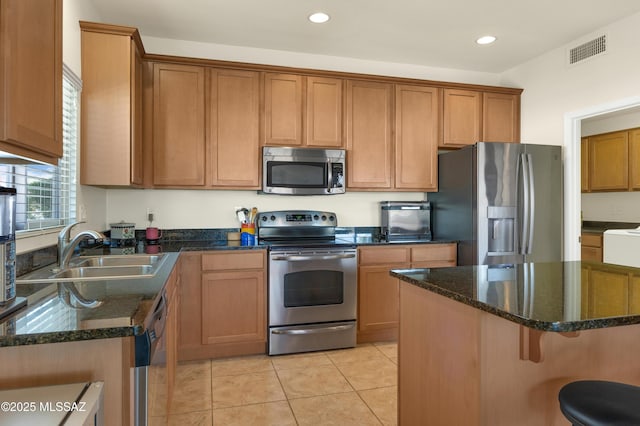 kitchen with dark stone countertops, sink, light tile patterned floors, and stainless steel appliances