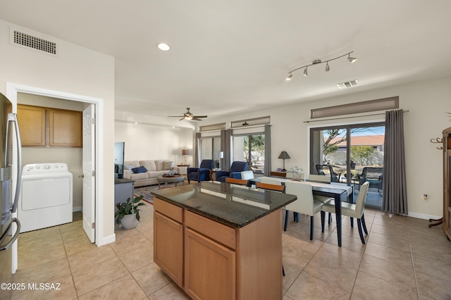 kitchen with light tile patterned flooring, washer / dryer, dark stone counters, a center island, and ceiling fan