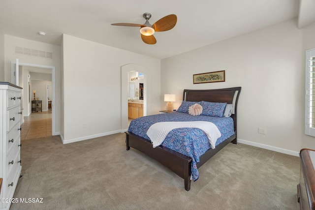 bedroom featuring ceiling fan, light colored carpet, and connected bathroom