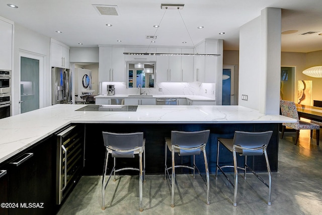 kitchen with light stone counters, a breakfast bar area, white cabinets, and appliances with stainless steel finishes