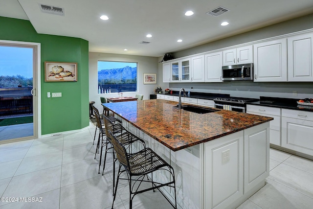 kitchen with sink, light tile patterned floors, appliances with stainless steel finishes, white cabinetry, and an island with sink