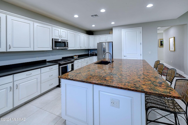 kitchen featuring stainless steel appliances, an island with sink, a breakfast bar, and white cabinetry