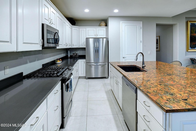 kitchen with sink, light tile patterned floors, appliances with stainless steel finishes, dark stone counters, and white cabinets