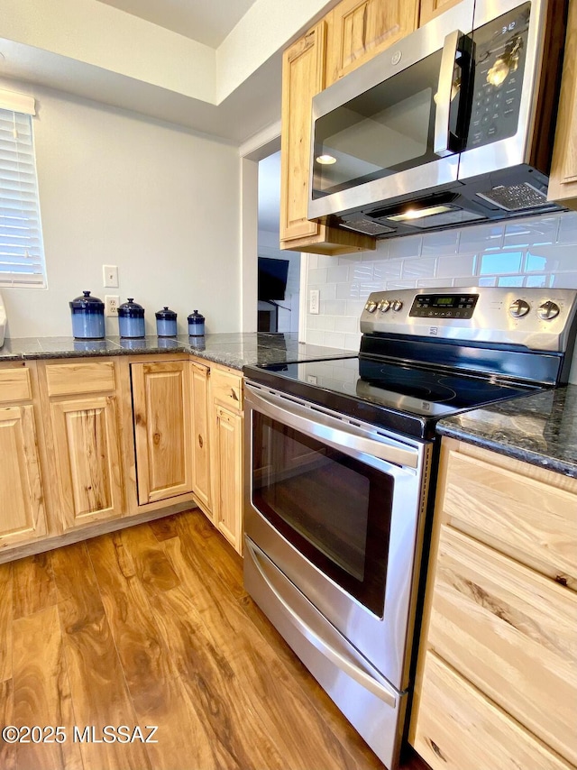 kitchen featuring tasteful backsplash, dark stone countertops, stainless steel appliances, light brown cabinets, and light hardwood / wood-style flooring